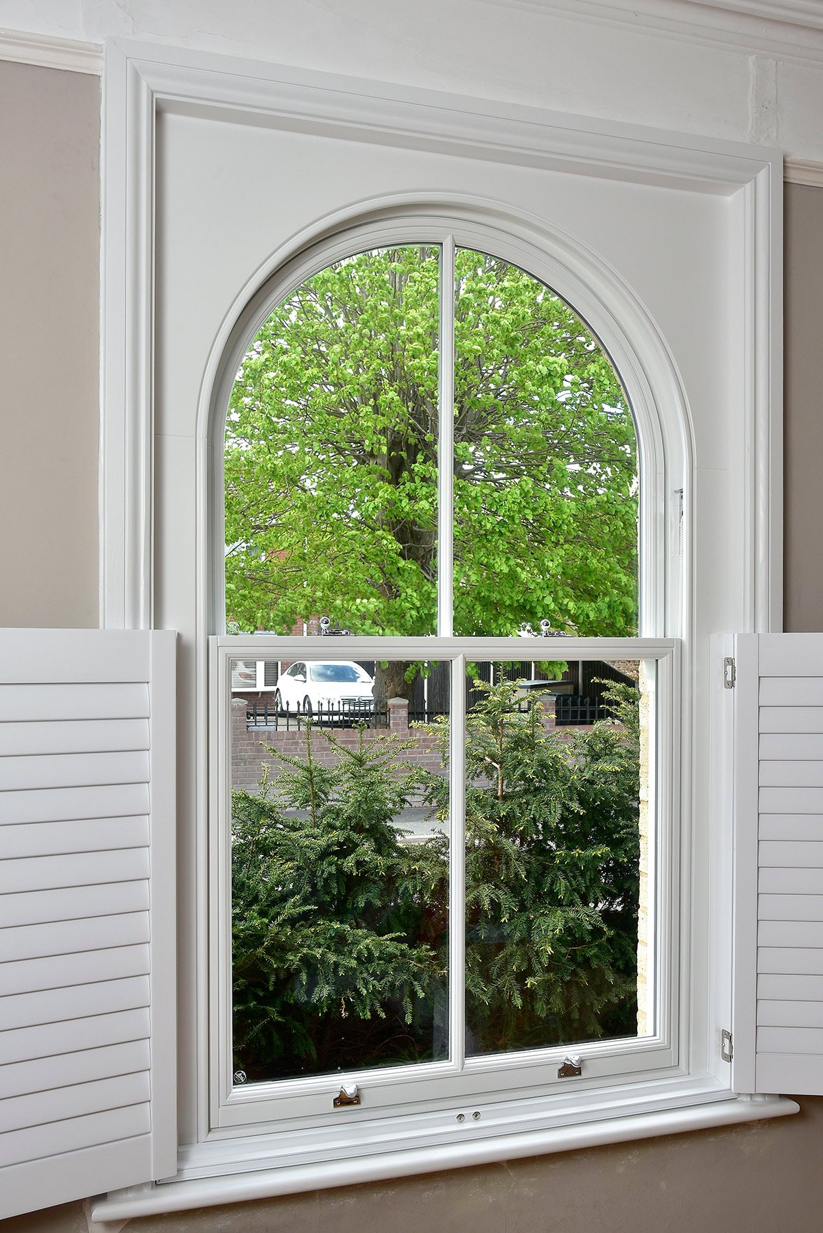 a white arched sash window with open wooden shutters