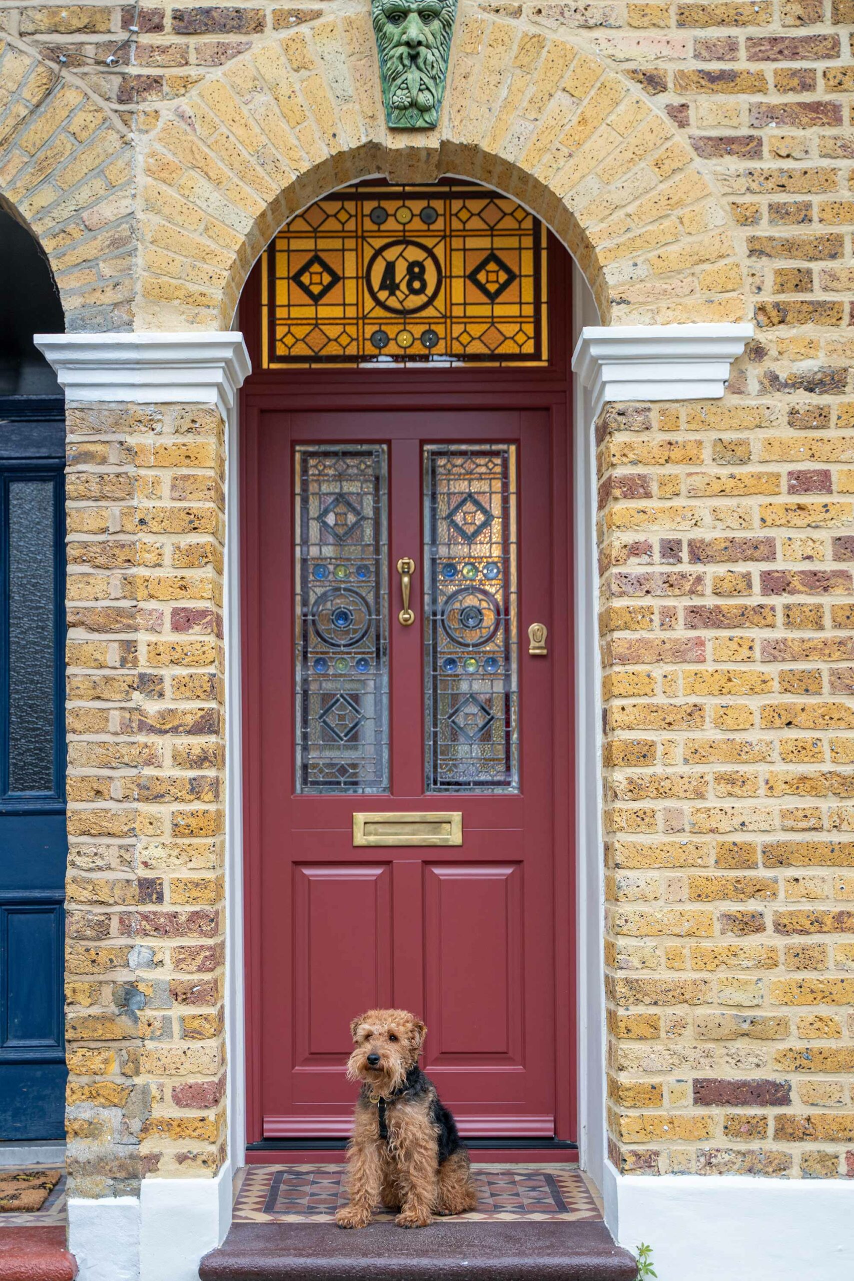 a red door on a terraced home with stained glass and a dog sat in front